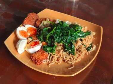 Üzerinde ıspanak, haşlanmış yumurta ve ahşap masada servis edilen kızarmış balık köftesi olan bir tabak hazır şehriye.