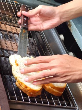 Two slices of bread, likely Roti Bakar or Indonesian grilled bread, are being grilled on a charcoal grill. The bread is spread with butter or margarine and possibly cheese or another topping. clipart