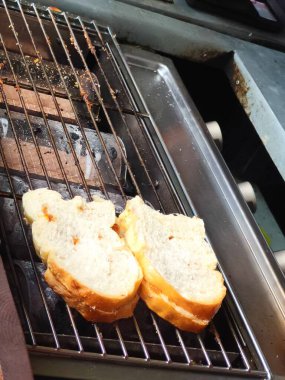 Muhtemelen Roti Bakar veya Endonezya usulü ızgara ekmek olmak üzere iki dilim ekmek mangalda kızartılıyor. Ekmek tereyağı, margarin ve muhtemelen peynir ya da başka bir malzemeyle yayılır..