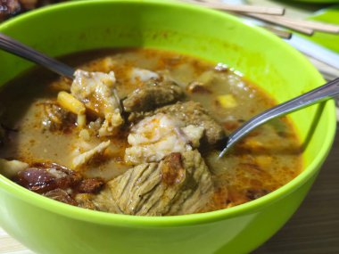 A bowl of hearty Gulai Kambing, a rich Indonesian soup brimming with tender goat meat, vegetables, and spices. Served hot on the table. clipart