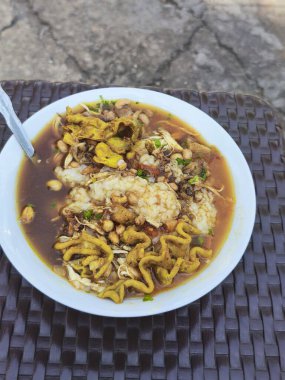 A bowl of Bubur Ayam, a comforting Indonesian chicken porridge with savory broth, shredded chicken, and various toppings like peanuts, crackers, and scallions. clipart