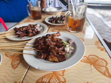 Sate Kambing ya da keçi satay ziyafeti bekliyor. Dilimlenmiş soğan ve ferahlatıcı buzlu çayla yenmeye hazır..