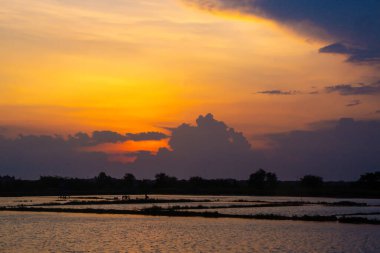 Dramatik bir gökyüzü ve siluetli figürler günbatımında çarpıcı bir sahne yaratır..