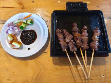 Baharatlı keçi eti şişi ya da sıcak bir tabakta satay yanında taze sebze ve sosla birlikte..