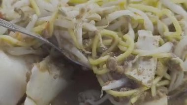 Gümüş kaşıkla, bir insan taze fasulye filizlerini ve geleneksel Bogor toge goreng yemeğinin aromalı sosunu nazikçe karıştırarak lezzetli bir yemek hazırlar..