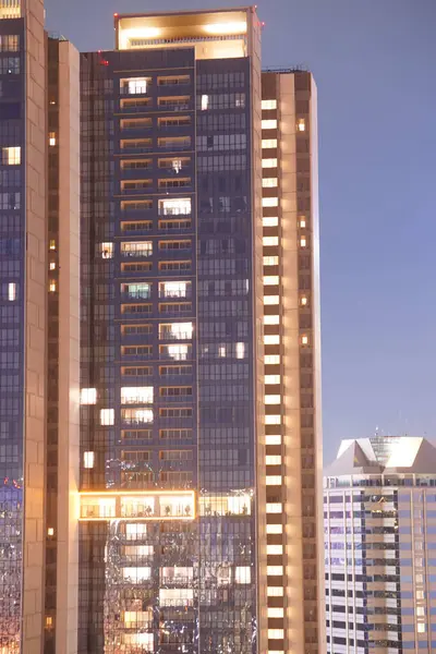 Kalabalık şehir siluetinin gece manzarası. Yüksek bir gökdelen çerçevenin sağ tarafına hükmediyor. Aydınlatılmış pencereleri karanlık gece gökyüzü ile çelişen ızgara benzeri bir desen oluşturuyor..