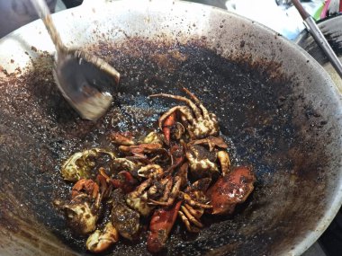 Açık ateşte pişen kırmızı renkli yengeçlerle dolu büyük bir tava. Aşçı yengeçleri büyük bir kaşıkla karıştırıyor..