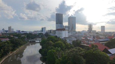 Huzurlu bir nehir bir şehir manzarası boyunca yol alır, ufuk çizgisini yansıtır ve huzur dolu bir an sunar. Surabaya, Endonezya.