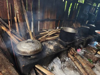 a glimpse into a rustic Indonesian kitchen, filled with the warmth and energy of a bustling food preparation space. A large pot sits over a wood fire, steam rising from its contents, suggesting a hearty broth or stew is being cooked. clipart