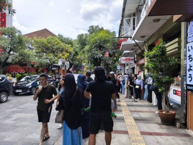 January 29, 2025. Bandung, Indonesia. A lively scene on Jalan Braga, bustling with traffic and pedestrians, featuring a colorful tour bus amidst the festive atmosphere of Chinese New Year celebrations clipart