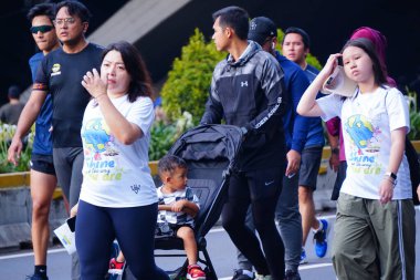 16 Şubat 2025. Jakarta, Endonezya. Jalan Sudirman 'ın Arabasız Günü' nden canlı bir sahne, çeşitli katılımcılar renkli atletizm kıyafetleriyle koşuyor ve temiz havanın tadını çıkarıyor..