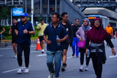 February 16, 2025. Jakarta, Indonesia. A vibrant scene from Car Free Day on Jalan Sudirman, showcasing diverse participants jogging and enjoying the fresh air in colorful athletic wear. clipart