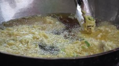 Tempe Mendoan 'ın yakın çekimi, Endonezya' nın geleneksel tempeh 'i, kızgın yağda kızartılıyor, köpüren ve cızırdayan dokular sergiliyor, hamur parçaları maşayla kaldırılıyor..