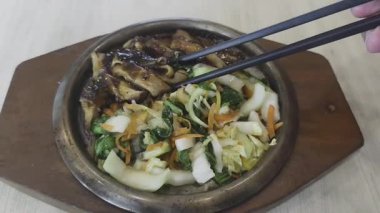 Japon yemeklerini karıştırmak için çubuk kullanan bir insanın yakın plan fotoğrafı. Teriyaki soslu ve sebzeli ızgara tavuk parçaları..