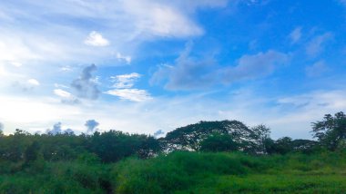 Batı Surabaya, Endonezya 'da bereketli yeşillikler, dağınık ağaçlar, uzak bir bina ve görünen uydusu olan berrak mavi bir gökyüzü içeren sakin bir manzara..