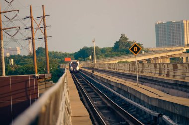 Modern bir LRT treni, Jakarta yakınlarında önemli bir hız limiti tabelasının yer aldığı şehir manzaralı yüksek bir pistte seyahat eder..