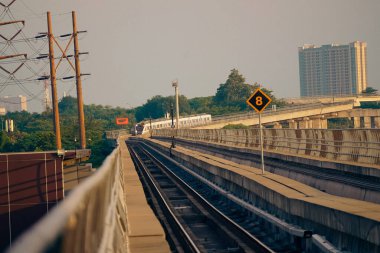 Modern bir LRT treni, Jakarta yakınlarında önemli bir hız limiti tabelasının yer aldığı şehir manzaralı yüksek bir pistte seyahat eder..