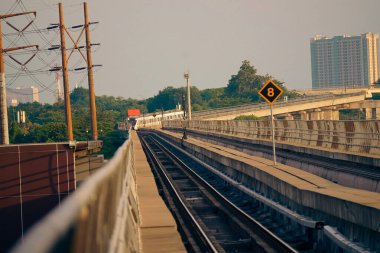 Modern bir LRT treni, Jakarta yakınlarında önemli bir hız limiti tabelasının yer aldığı şehir manzaralı yüksek bir pistte seyahat eder..