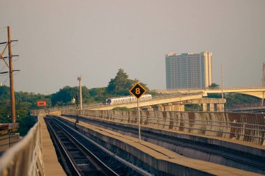 Modern bir LRT treni, Jakarta yakınlarında önemli bir hız limiti tabelasının yer aldığı şehir manzaralı yüksek bir pistte seyahat eder..