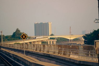 Modern bir LRT treni, Jakarta yakınlarında önemli bir hız limiti tabelasının yer aldığı şehir manzaralı yüksek bir pistte seyahat eder..