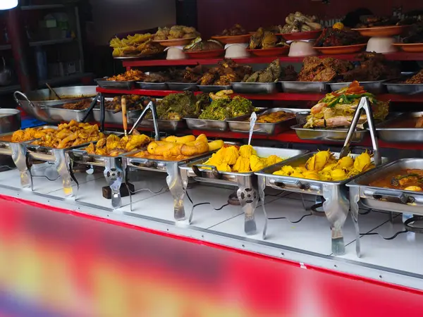 Padang Gıda açık büfesinde çeşitli metal tepsilerde pişirilmiş yemekler, zengin baharatlar ve çeşitli dokular sergileniyor, tipik Güneydoğu Asya mutfağı..