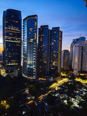 Jakarta 'nın canlı şehir manzarası alacakaranlıkta aydınlık gökdelenler, parlayan bir günbatımı gökyüzü ve aşağıdaki hareketli şehir caddeleri.
