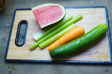 Çeşitli kesilmiş sebzeler ve karpuz parçaları ahşap bir kesme tahtasına dizilmiştir.