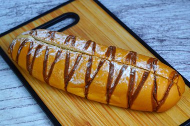 Çikolata serpiştirilmiş kahverengi moka somunu ve pudra şekeri, ahşap bir kesme tahtasının üzerinde dinleniyor..