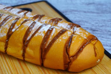 Çikolata serpiştirilmiş kahverengi moka somunu ve pudra şekeri, ahşap bir kesme tahtasının üzerinde dinleniyor..