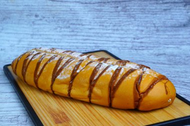 Çikolata serpiştirilmiş kahverengi moka somunu ve pudra şekeri, ahşap bir kesme tahtasının üzerinde dinleniyor..