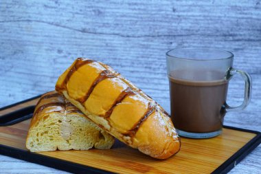 Dilimlenmiş bir moka altın somunu çikolatalı çiseleme ve pudra şekerli, tahtanın üzerinde bir bardak sıcak çikolatayla servis edilir..