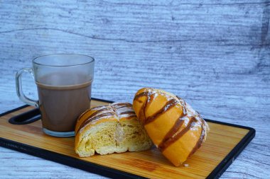 Dilimlenmiş bir moka altın somunu çikolatalı çiseleme ve pudra şekerli, tahtanın üzerinde bir bardak sıcak çikolatayla servis edilir..