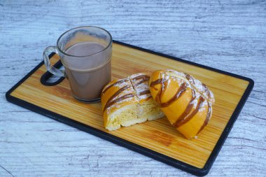 Dilimlenmiş bir moka altın somunu çikolatalı çiseleme ve pudra şekerli, tahtanın üzerinde bir bardak sıcak çikolatayla servis edilir..