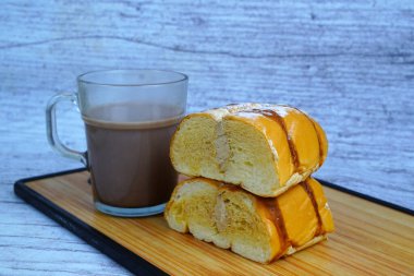 Çikolatalı ve pudra şekerli dilimlenmiş altın ekmeğin yanında bir kupa sütlü kahve kreması..