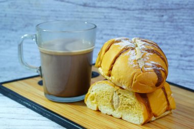 Çikolatalı ve pudra şekerli dilimlenmiş altın ekmeğin yanında bir kupa sütlü kahve kreması..