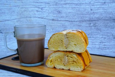 Çikolatalı ve pudra şekerli dilimlenmiş altın ekmeğin yanında bir kupa sütlü kahve kreması..