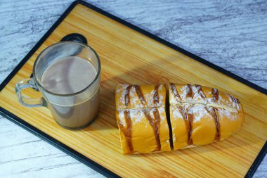 Dilimlenmiş bir moka altın somunu çikolatalı çiseleme ve pudra şekerli, tahtanın üzerinde bir bardak sıcak çikolatayla servis edilir..