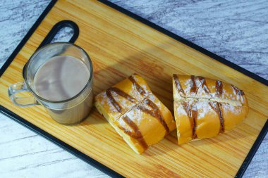 Dilimlenmiş bir moka altın somunu çikolatalı çiseleme ve pudra şekerli, tahtanın üzerinde bir bardak sıcak çikolatayla servis edilir..