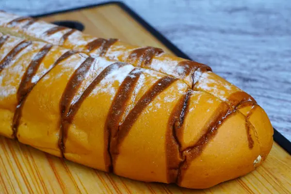 Çikolata serpiştirilmiş kahverengi moka somunu ve pudra şekeri, ahşap bir kesme tahtasının üzerinde dinleniyor..