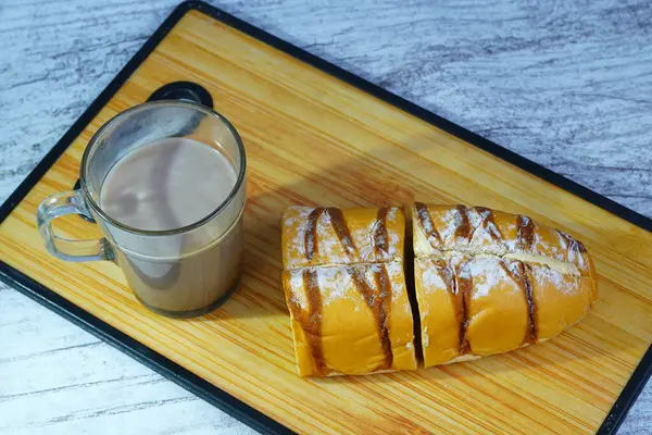 Dilimlenmiş bir moka altın somunu çikolatalı çiseleme ve pudra şekerli, tahtanın üzerinde bir bardak sıcak çikolatayla servis edilir..