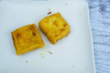 İki altın renginde tofu karesi beyaz dikdörtgen bir tabakta otururlar..