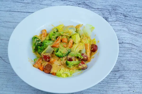 Kızarmış sebze ve kremalı sosis karışımı, beyaz bir tabakta sunuluyor..