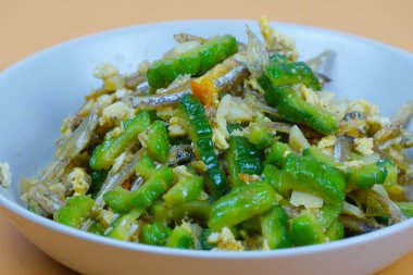 Hafif turuncu arka planda, beyaz bir kasede servis edilen, ançüez ve yumurtalı canlı kızarmış kavun..