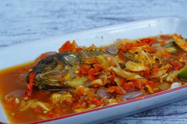 Pecak Ikan Mujair ya da kızarmış tilapia canlı, baharatlı ve ekşi Endonezya biberine batırılmış soğan ve kireç ile birlikte beyaz bir tabakta servis edilir..
