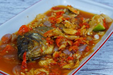 Pecak Ikan Mujair ya da kızarmış tilapia canlı, baharatlı ve ekşi Endonezya biberine batırılmış soğan ve kireç ile birlikte beyaz bir tabakta servis edilir..
