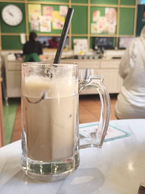 Kopi Tarık ya da Endonezya köpüğü, buzlu kahve çekti, siyah bir pipetle bir fincanda servis etti, bulanık bir arka planda bir insanın.