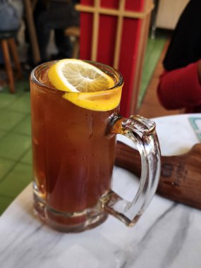 ferahlatıcı bir bardak buzlu limon çayı, parlak sarı bir limon dilimiyle süslenmiş, kapalı bir mermer masaya kurulmuş..