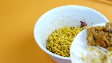 Tavuk yağı ve baharatlı erişteler yemek çubuklarıyla beyaz bir kasede karıştırılıyor..