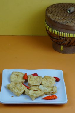 Birkaç parça kızarmış tofunun yakın çekimi, yaygın bir Endonezya aperatifi, kırmızı biberli beyaz bir tabakta portakal arka planında servis edilir..