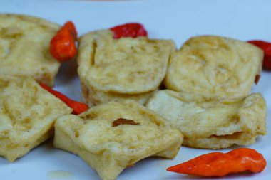 Birkaç parça kızarmış tofunun yakın çekimi, yaygın bir Endonezya aperatifi, kırmızı biberli beyaz bir tabakta portakal arka planında servis edilir..